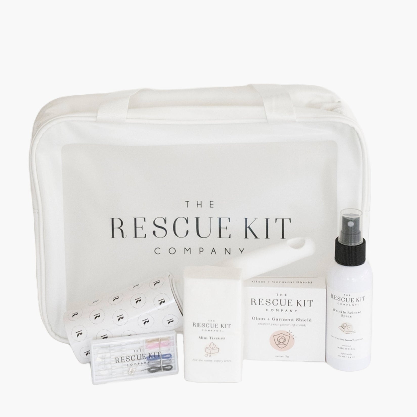 The Signature Bride Kit by The Rescue Kit Company, featuring a white carry bag surrounded by bridal emergency essentials including sprays, lint roller, tissues, pins, tape, and chafe balm.