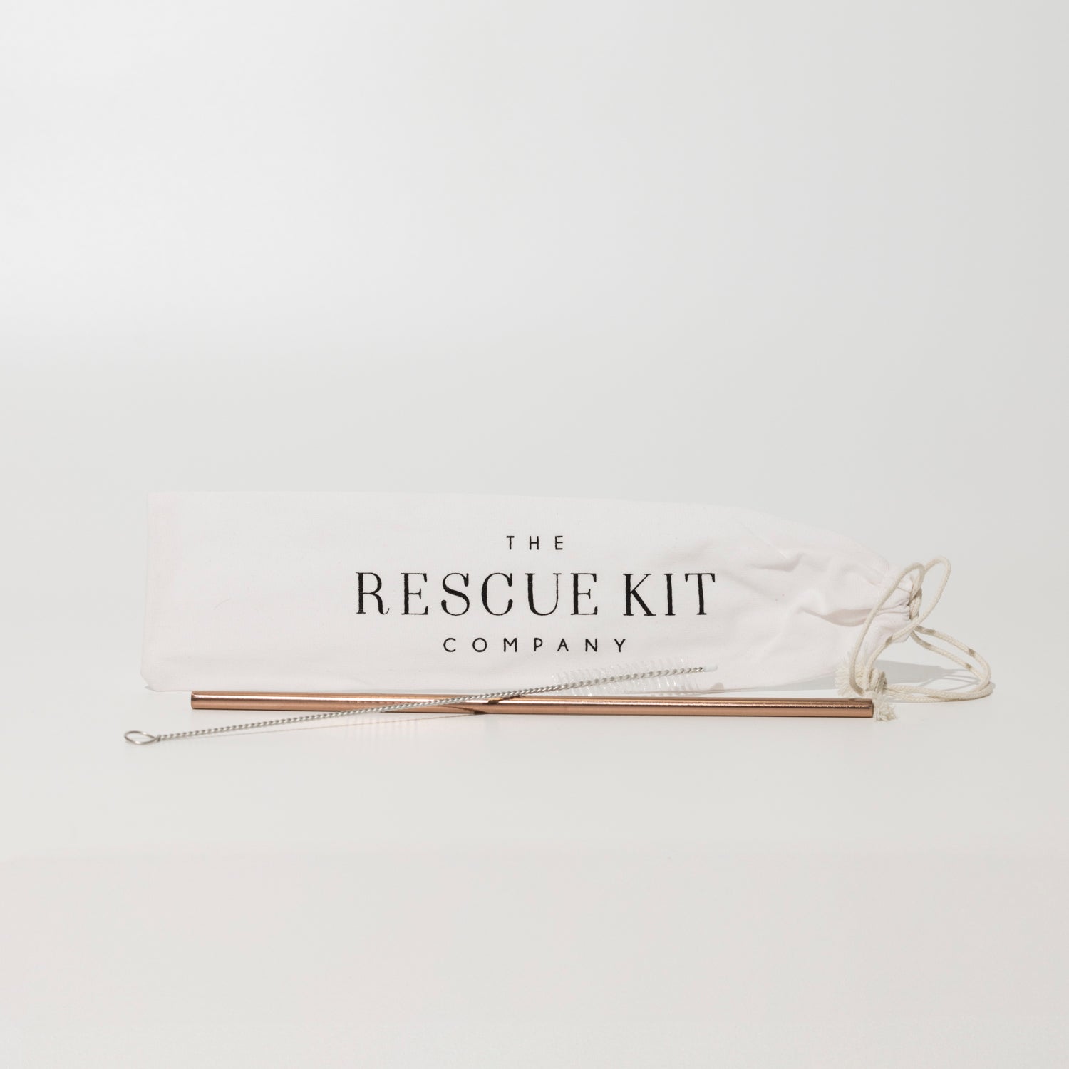 Reusable rose gold metal straw with cleaning brush, displayed in front of a white drawstring pouch featuring The Rescue Kit Company logo.