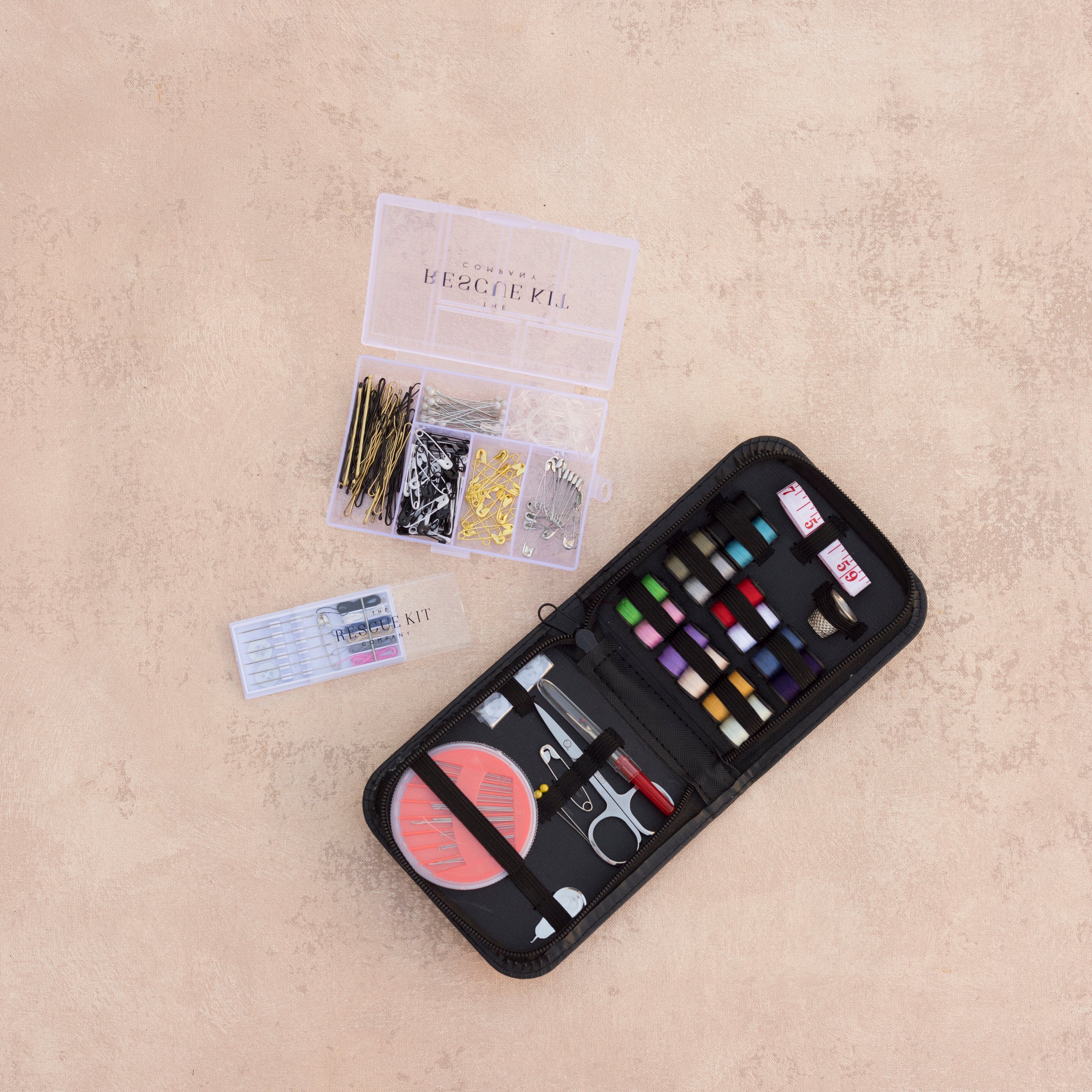 The Sewing Kit Trio by The Rescue Kit Company, containing a travel sewing kit, pre-threaded needles, and a hair + pin kit, shown open to see contents inside.