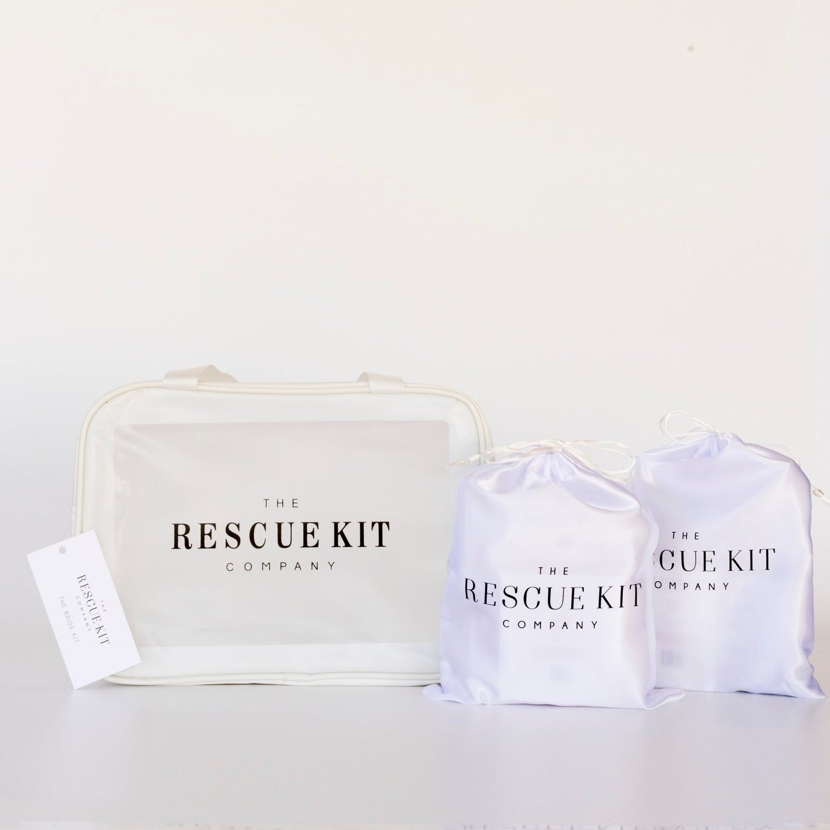 The Rescue Kit Company Photo Shoot Kit displayed with one large clear carry bag and two smaller white satin drawstring pouches, all featuring branded logos.