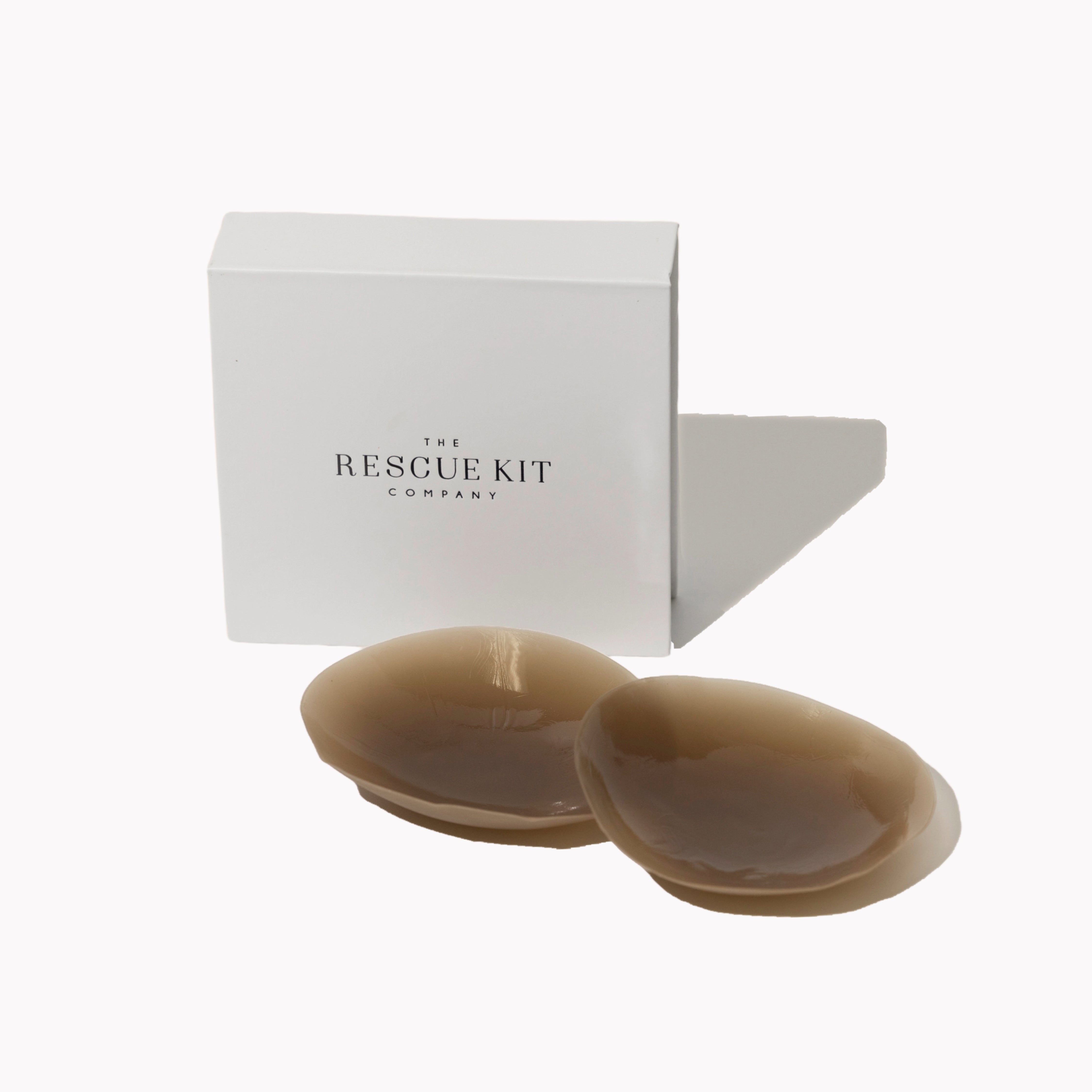 Silicone pasties by The Rescue Kit Company. Two pasties, dark skin tone color, outside their white custom packaging box.