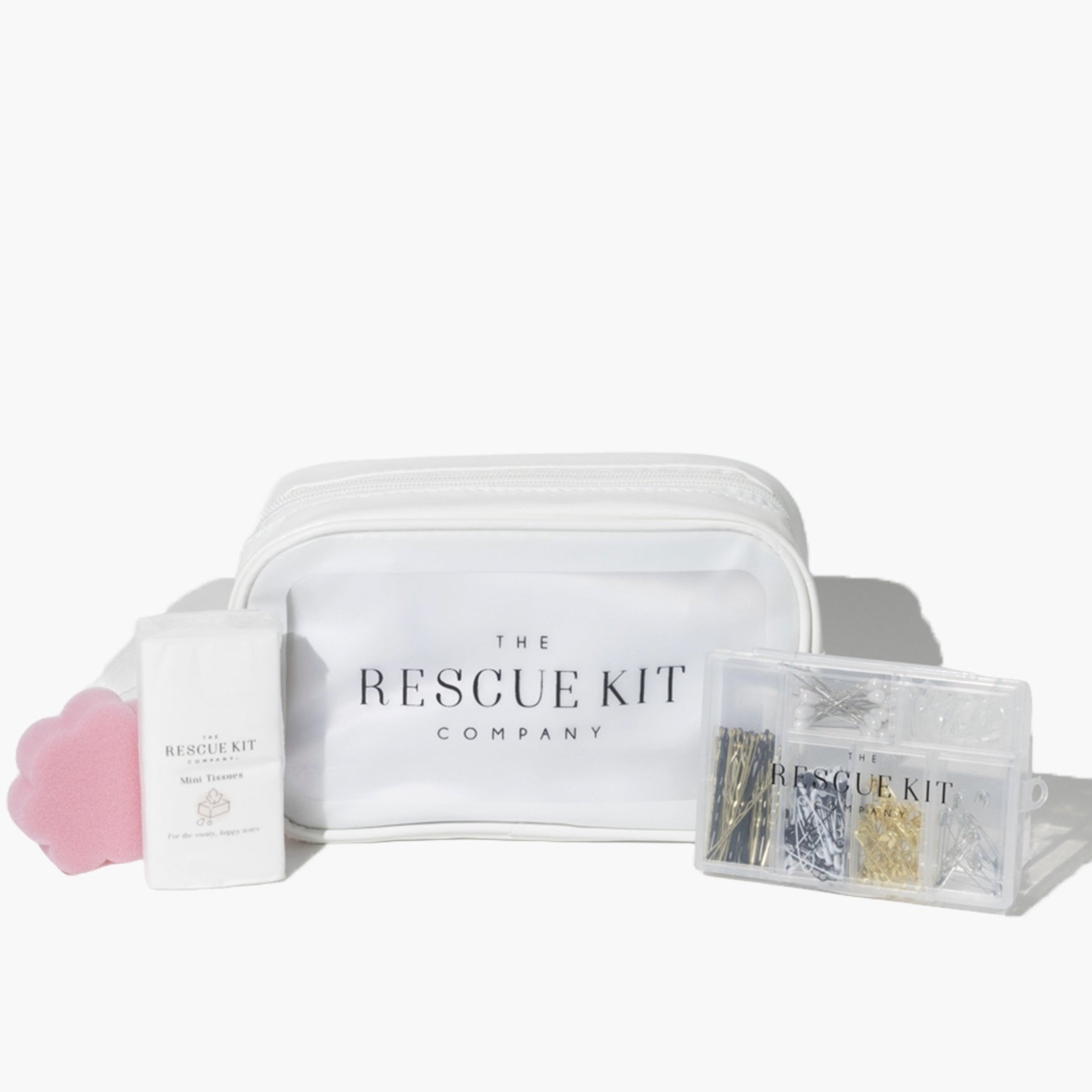 The Essential Bride Kit by The Rescue Kit Company, featuring a white cosmetic pouch, mini tissues, a pink flower-shaped sponge, and a clear container of pins and fashion tools.