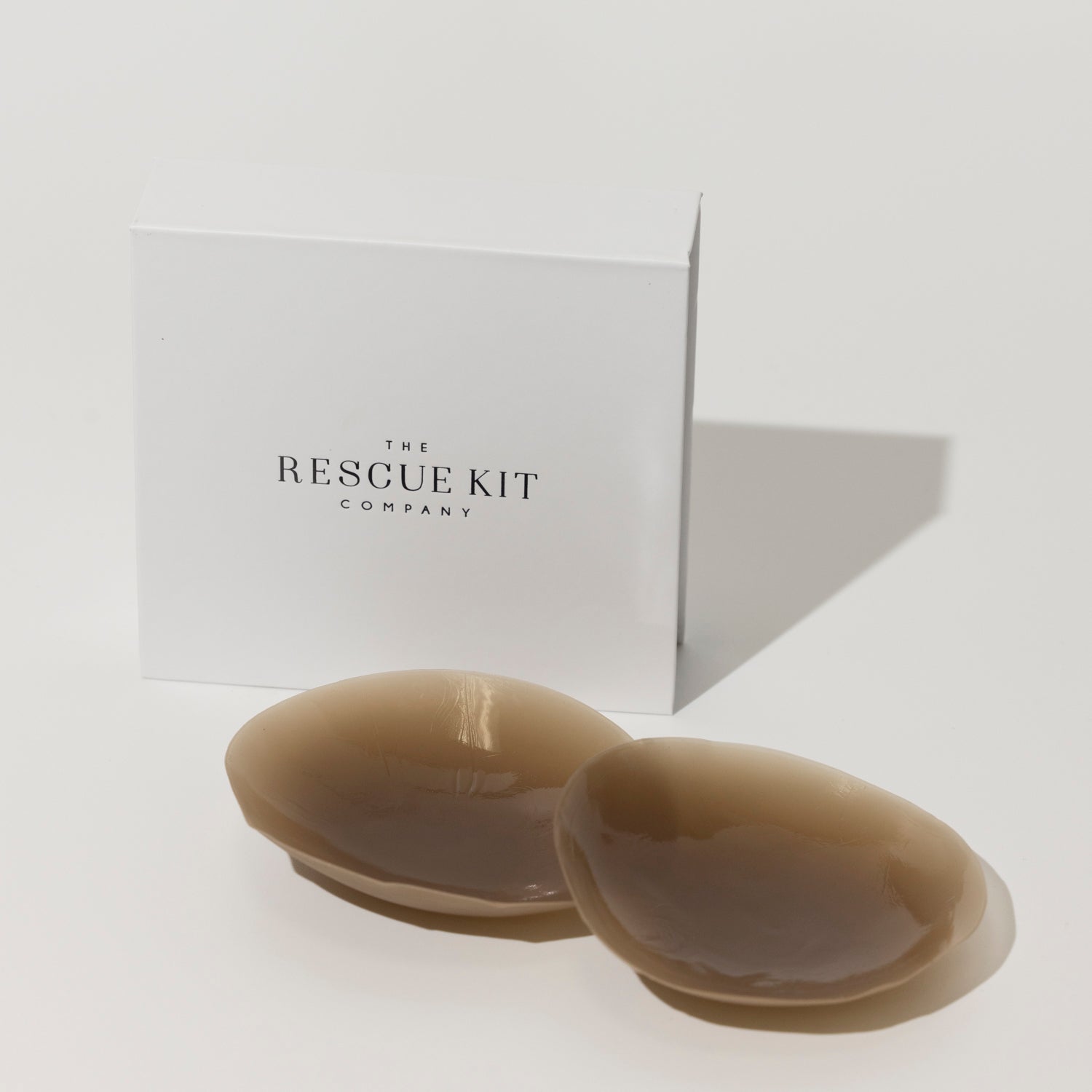 Silicone pasties by The Rescue Kit Company. Two pasties, dark skin tone color, outside their white custom packaging box.