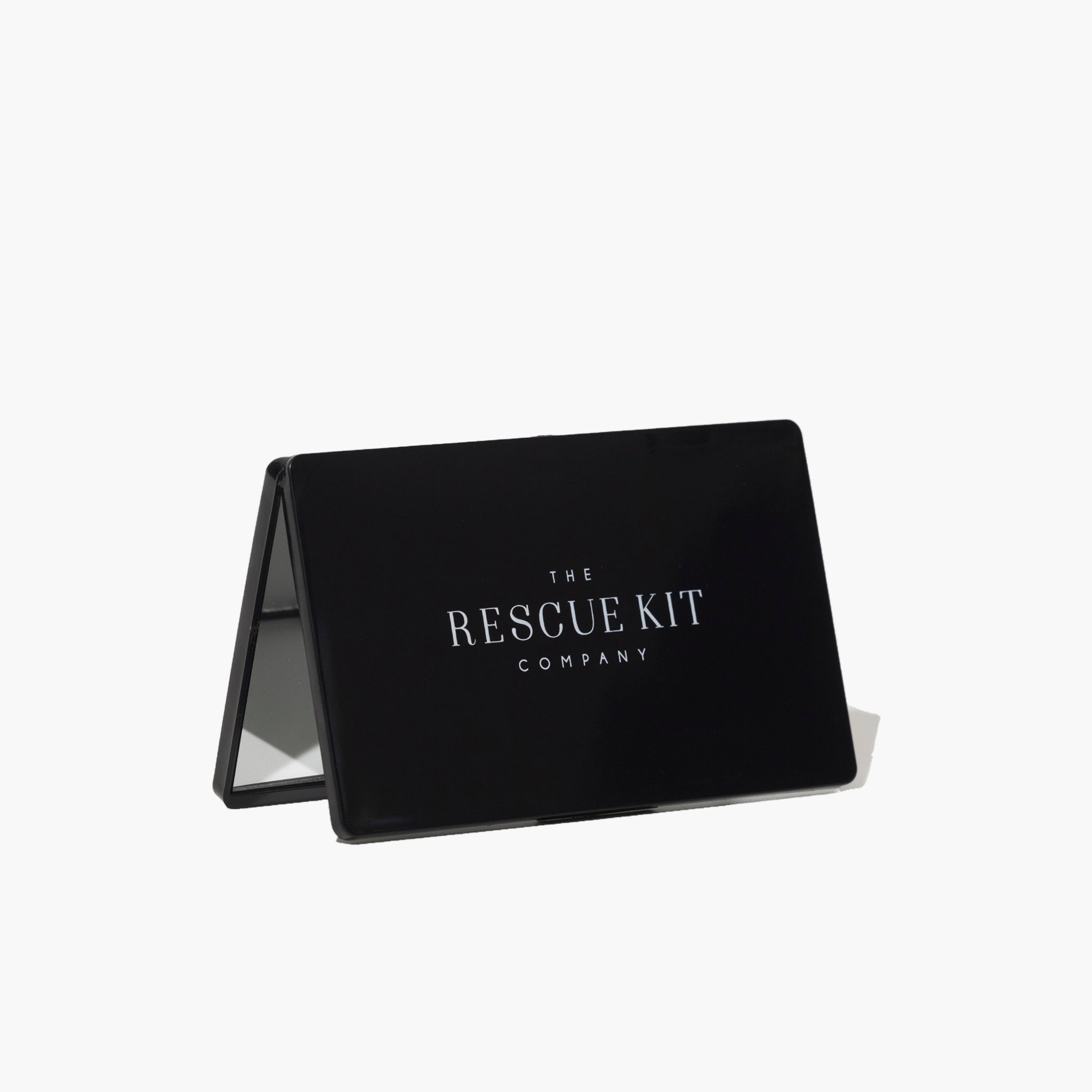 Black foldable vanity mirror with The Rescue Kit Company logo displayed on the front, propped open to reveal its compact, travel-friendly design.