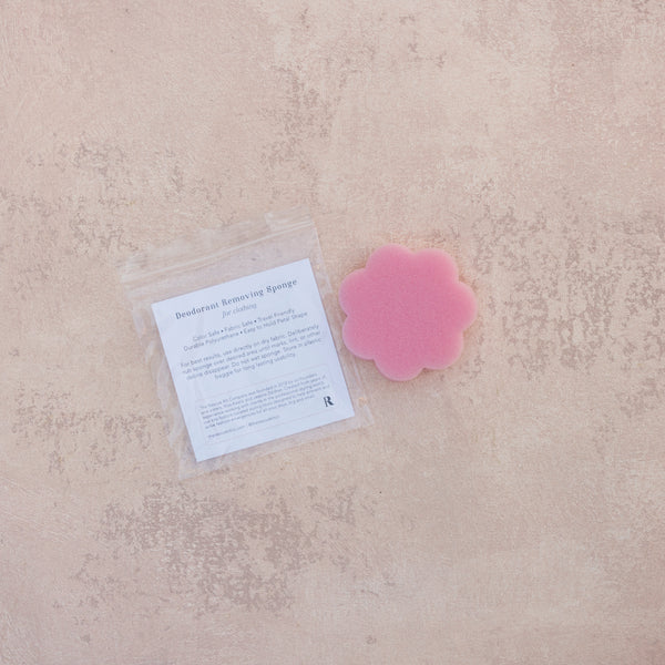 Pink, flower shaped deodorant removing sponge by The Rescue Kit Company. Designed to remove deodorant marks from clothing. Shown in use on a black top.