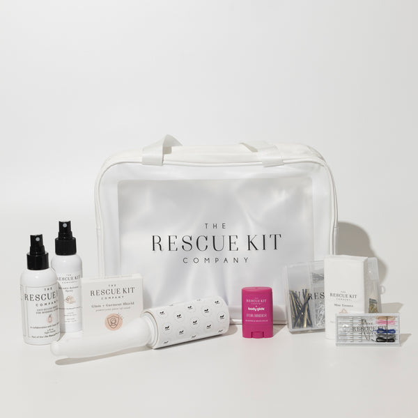 The Bride Kit by The Rescue Kit Company, featuring a white carry bag surrounded by bridal emergency essentials including sprays, lint roller, tissues, pins, tape, and chafe balm.