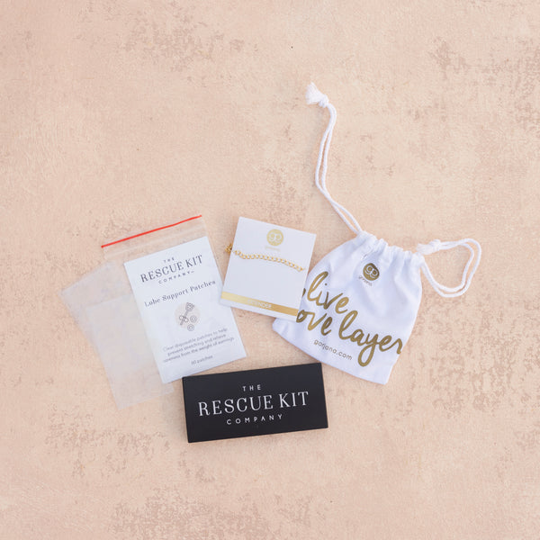 The accessory trio from The Rescue Kit Company containing lobe support patches, a 3" gold necklace extender by Gorjana, and a black compact mirror.
