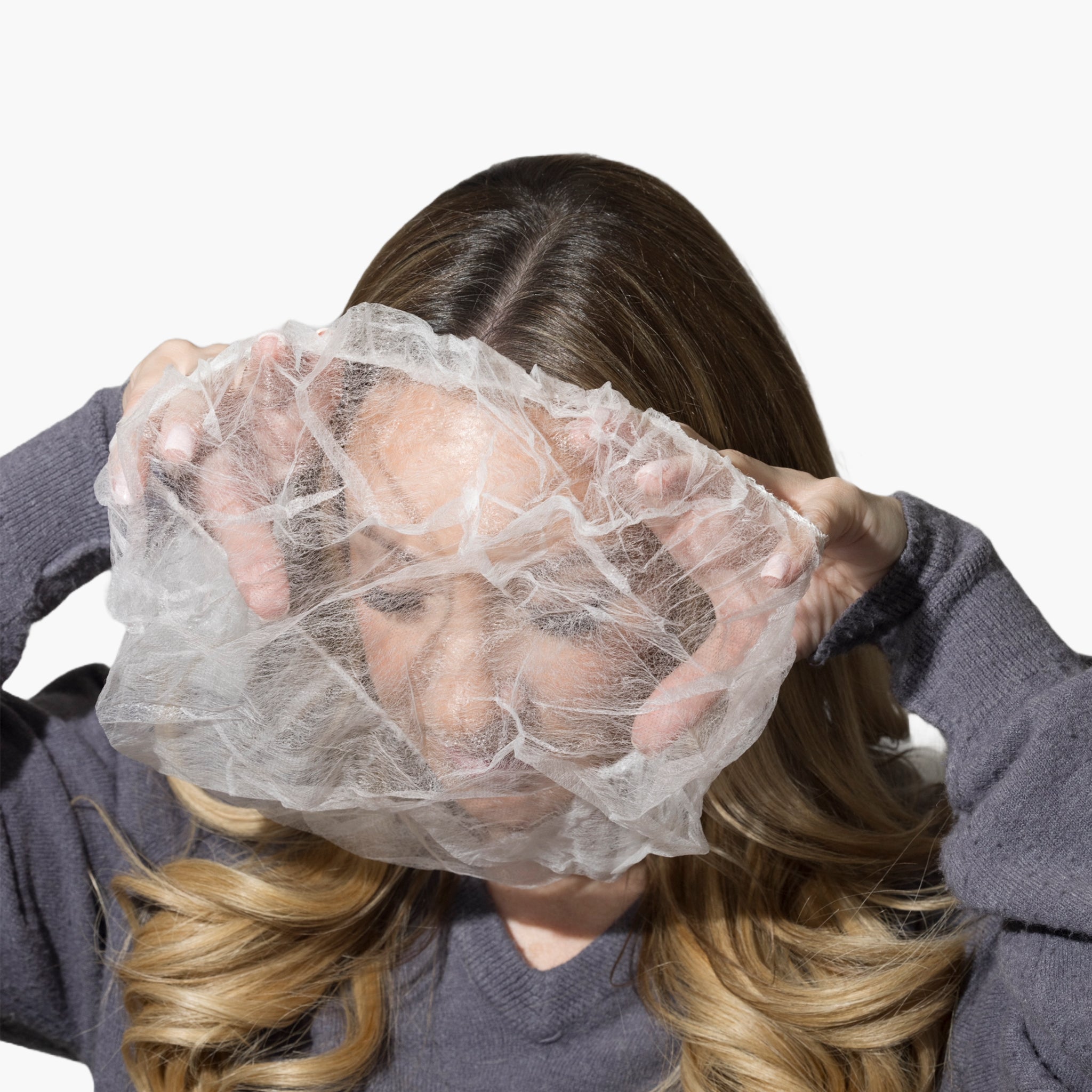 A lightweight, sheer protective covering for the hairline and face to prevent makeup transfer onto clothing, by The Rescue Kit Company. Picture shows the Glam + Garment Shield being used by model Risa Kostis.
