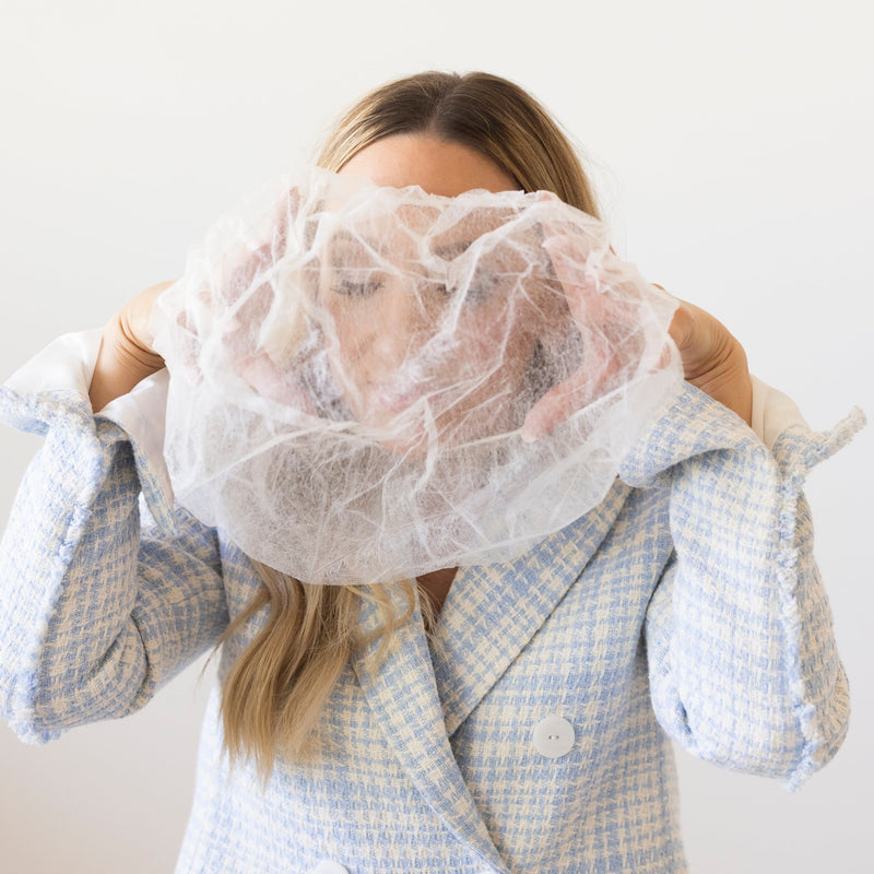 A lightweight, sheer protective covering for the hairline and face to prevent makeup transfer onto clothing, by The Rescue Kit Company. Picture shows the Glam + Garment Shield being used by model Risa Kostis.