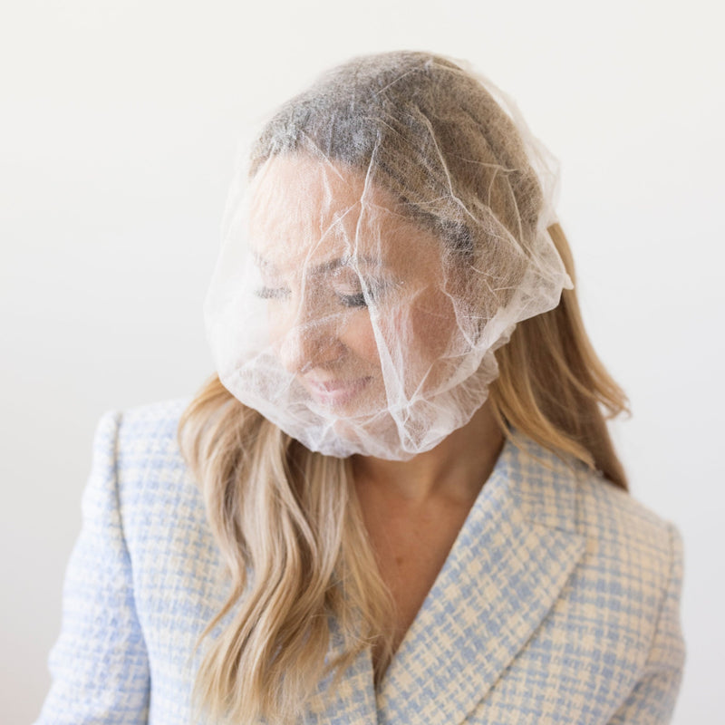 A lightweight, sheer protective covering for the hairline and face to prevent makeup transfer onto clothing, by The Rescue Kit Company. Picture shows the Glam + Garment Shield being used by model Risa Kostis.