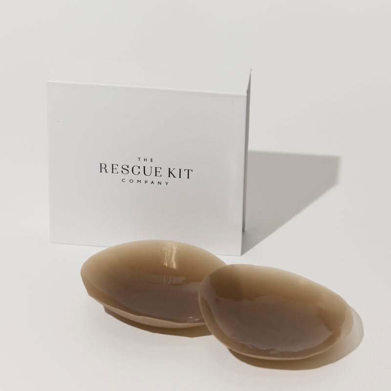Silicone pasties by The Rescue Kit Company. Two pasties, dark skin tone color, outside their white custom packaging box.
