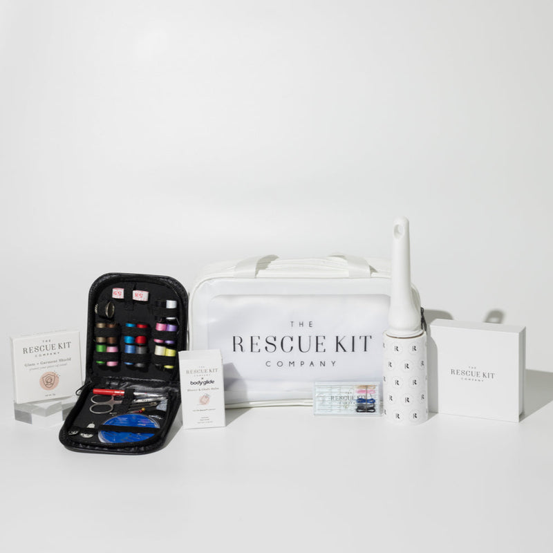 The Bridesmaid Kit by The Rescue Kit Company, featuring a white cosmetic bag, glam + garment shield, body glide, lint roller, mini hair + pin kit, and an open sewing kit with multicolored threads and styling tools.