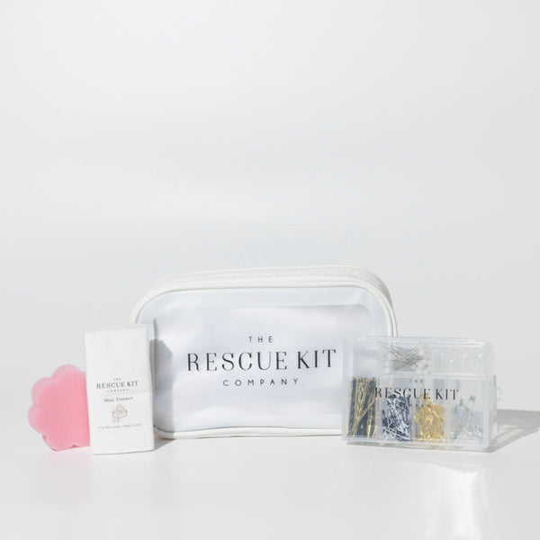 The Essential Bride Kit by The Rescue Kit Company, featuring a white cosmetic pouch, mini tissues, a pink flower-shaped sponge, and a clear container of pins and fashion tools.
