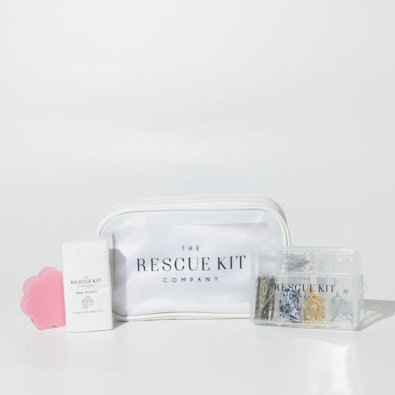 The Essential Bride Kit by The Rescue Kit Company, featuring a white cosmetic pouch, mini tissues, a pink flower-shaped sponge, and a clear container of pins and fashion tools.