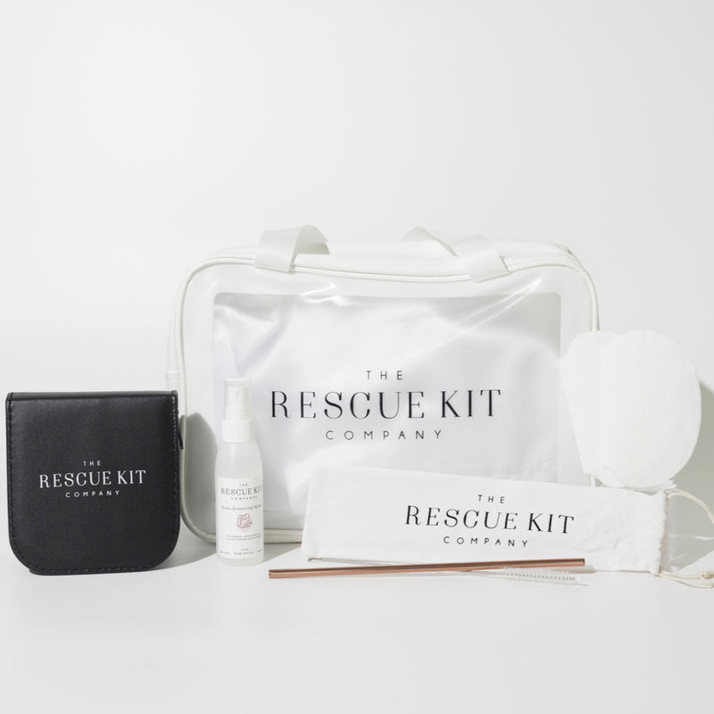 The Rescue Kit Company's Photo Shoot Kit, featuring a white cosmetic bag, stain removing spray, black leather sewing kit, underarm sweat pads, and reusable metal straw with cleaning brush in branded pouch.